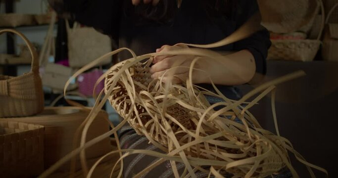 An Asian female artisan who is a rural villager weaving folk women's baskets and bags made from leftover paper band to sell as extra income in the community shop.