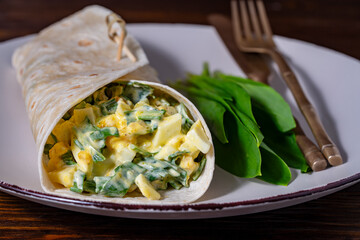 Homemade burrito wraps with boiled eggs, potato, green wild garlic and sour cream for healthy breakfast on plate, closeup - 783627643