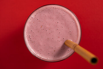 Raspberry banana smoothie in glass on a red background, closeup, top view