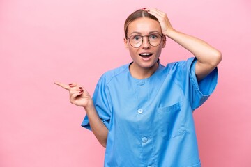Young nurse doctor woman isolated on pink background surprised and pointing finger to the side