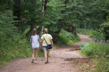 Obraz premium Back view of two women walking through footpath surrounded by growing dense trees
