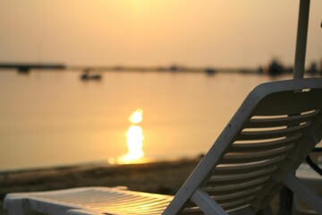 Deck chair in background of sea during sunset