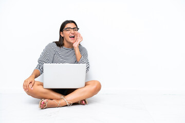 Young caucasian woman with a laptop sitting on the floor shouting with mouth wide open