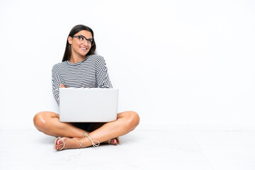 Young caucasian woman with a laptop sitting on the floor looking up while smiling