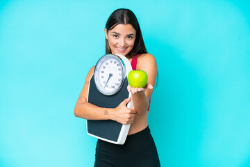 Young caucasian woman isolated on blue background holding weighing machine and offering an apple