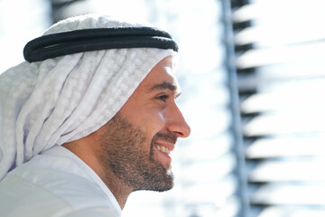 Profile of a smiling man in traditional Emirati attire, his face lit by the warmth of sunlight,...
