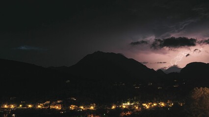 Scenic view of a village on slope of a green mountain range during lightning at night