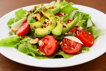 light salad. on a wooden table there is a white plate with avocado tomato and nut salad, top view, healthy concept