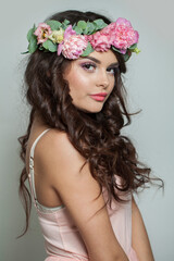 Happy summer woman with long dark wavy hair, clean shiny skin and pink flower crown, studio portrait. Cosmetic, happiness, beauty and fashion concept