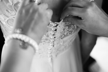 Black and white closeup of hands of a Bridesmaid helping the bride fasten corset for her wedding day