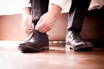 Closeup of hands of groom tying shoelaces on shoes - obrazy, fototapety, plakaty