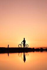 Vertical of cyclist silhouette near a pond at sunset with water reflection