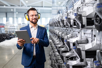 Industrial plant manager walking by production line machine and checking productivity.