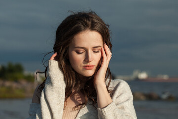 Lovely brunette woman with fresh skin, natural make-up and healthy wavy brown hair enjoying the sunny morning and sea air. Female model outdoor fashion portrait