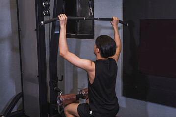 A skinny and lanky young man concentrates on lat pulldowns, focusing on back muscle development during his initial gym training session. - obrazy, fototapety, plakaty