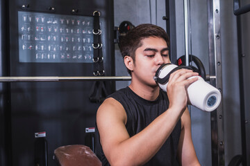 A young man enjoys a sip of cold water or sports drink from a insulated water bottle while sitting...