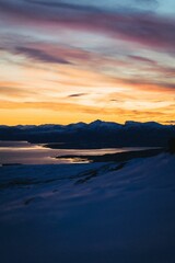 River and the rocky mountains covered with snow during scenic pink sunset, Tromso, Norway