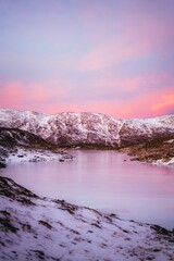 River and the rocky mountains covered with snow during pink sunset, Tromso, Norway