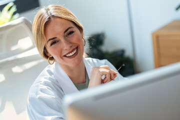 Beautiful smart nutritionist woman working with computer while looking at camera in the...