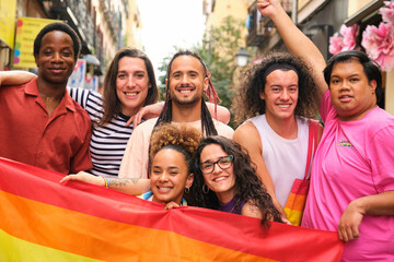 A group of people are posing for a picture with a rainbow flag. Scene is joyful and celebratory, as the group is likely participating in a pride event or celebration.
