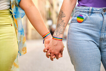 Unrecognizable lesbian couple holding hands with LGBTQ flag bracelets and pin. Pride Parade...