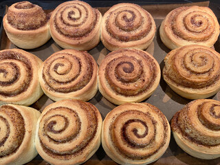 preparing homemade round cinnamon scrolls in a rectangular black baking pan
