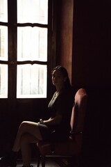 Vertical shot of a young caucasian woman sitting on a chair by a wooden door in a dark room