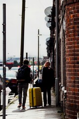 Vertical shot of a couple walking on the street sidewalk with a bright yellow suitcase
