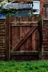 Vertical shot of an old wooden fence gate leading into a garden