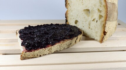 Closeup shot of the slice of bread with blackberry jam on top and loaf of bread next to it