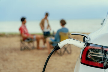 Alternative family vacation trip traveling by the beach with electric car recharging battery from...