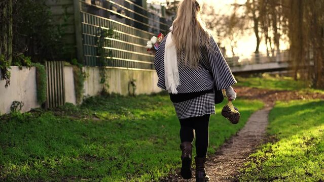 Rear footage of a woman in a checkered jacket walking at a park on blurred background