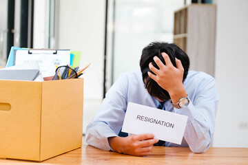 Man at desk with resignation letter, pondering his decision beside a packed box.