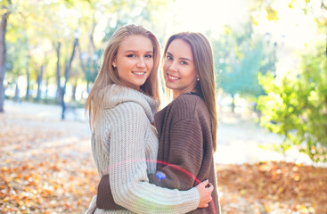 Fashionable beautiful young girlfriends walking together in the autumn park background. Having fun...