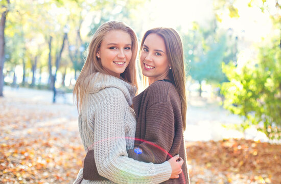 Fashionable beautiful young girlfriends walking together in the autumn park background. Having fun and posing.