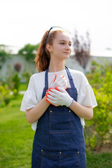 Side view of girl standing in garden, looking forward, wearing overalls and gloves. Concept of taking care of nature.