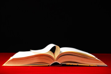 Pages of a thick book are turned on a red and black background, space for text.