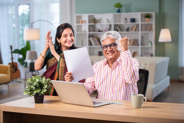 Indian asian retired couple accounting at home with laptop, papers, money and piggy bank
