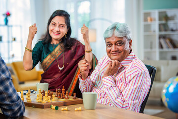 Mature Indian couple enjoying while playing chess board game together at home.