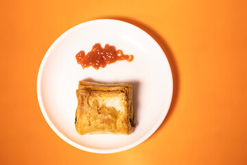 Vegetable puff with ketchup on white plate on orange background.