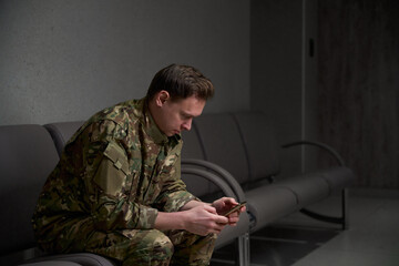 Serviceman reading news on his cellular phone in waiting area