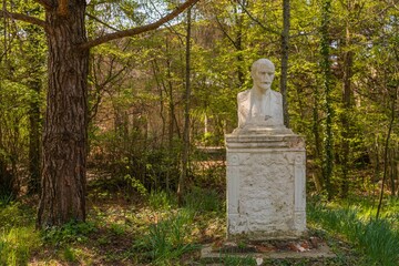 an old dilapidated plaster bust - a monument to the leader of the world proletariat surrounded by the first spring bright green foliage in an abandoned park on the Black Sea coast on a sunny day in Ap