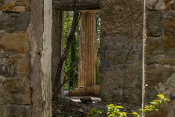 ruins of an old villa in the Greek style: a corridor and a column against the background of spring bright greenery on a sunny day