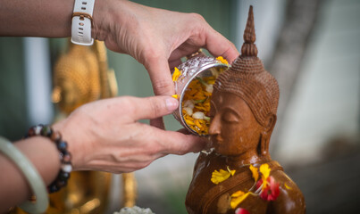 Songkran traditions in Thailand Thai Buddhists often take out Buddha statues in their homes and bathe them with Thai perfume and flowers on the first day of Songkran Festival. - obrazy, fototapety, plakaty