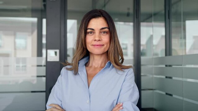 Confident smiling Latin professional middle aged elegant business woman corporate leader, happy mature female executive, lady manager standing in office crossing arms looking at camera, portrait.