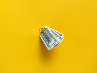 Hundred dollar bills poke out of a ragged hole in the yellow paper. Concept of income, salary, scholarship or donation. Financial cushion, credit and assistance.