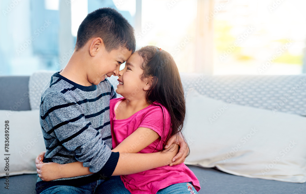 Wall mural Young, kids and happy with hugging, smile and joy in family home as children in youth. Siblings, cute and cuddle as brother and sister on couch for affection, love and childhood with noses touching