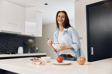 Happy woman preparing healthy meal in her kitchen, holding a bowl of delicious food in hands