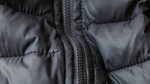 Black puffy winter jacket and zipper as a background close up, black background