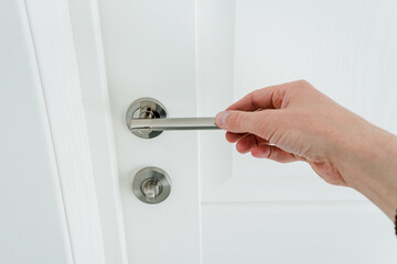 Hand holding door handle on white background, man opening snow-white door to room.